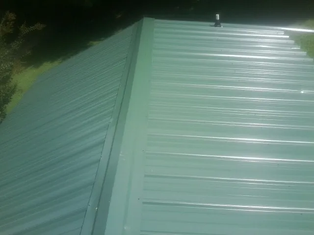 New green metal panels meeting at the ridge of a roof — Flat Roof Repair work by our crew in Newry