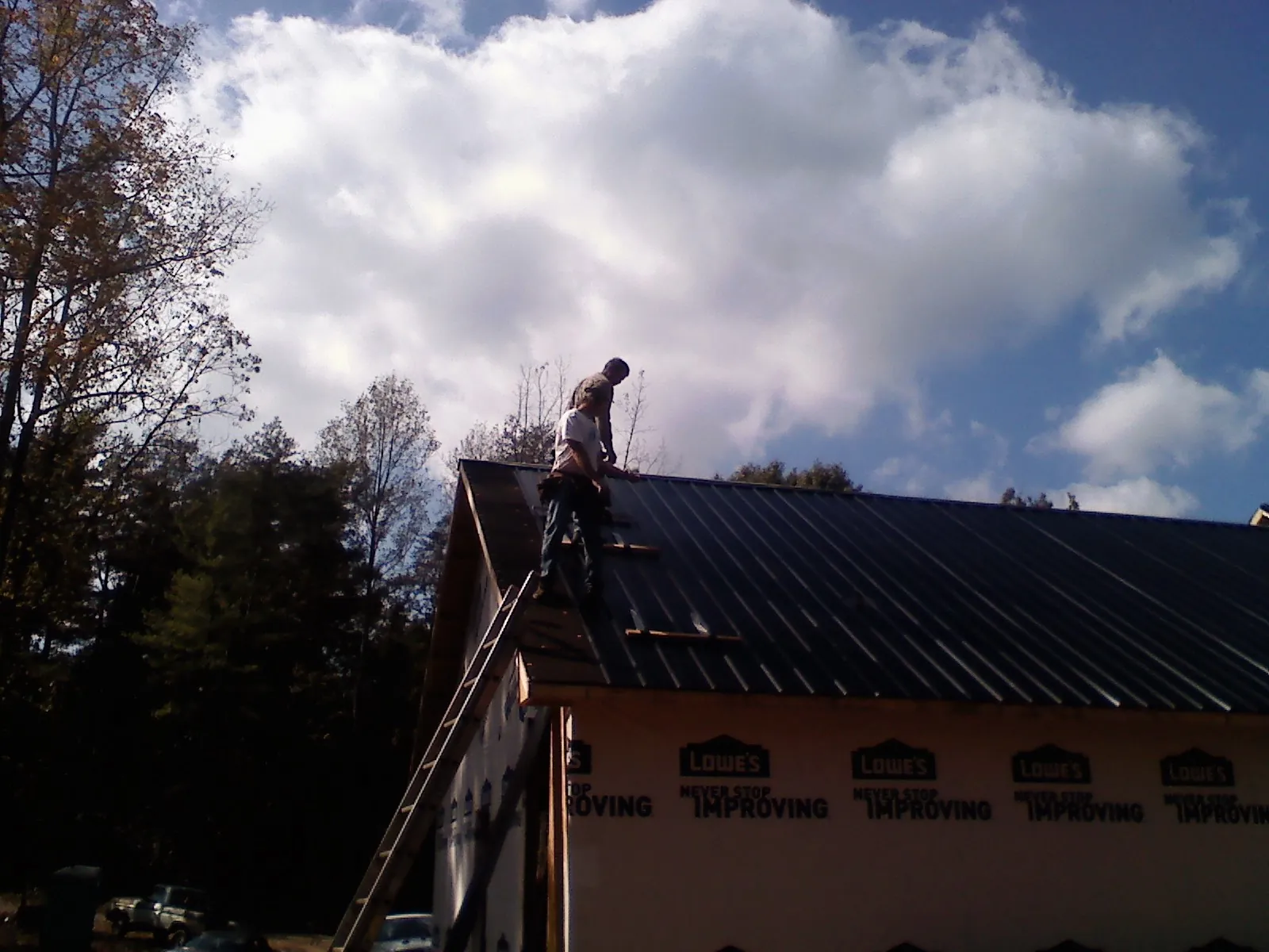 Roofer fastening dark metal panels high against a cloudy sky, from a Roof Inspection job in Newry