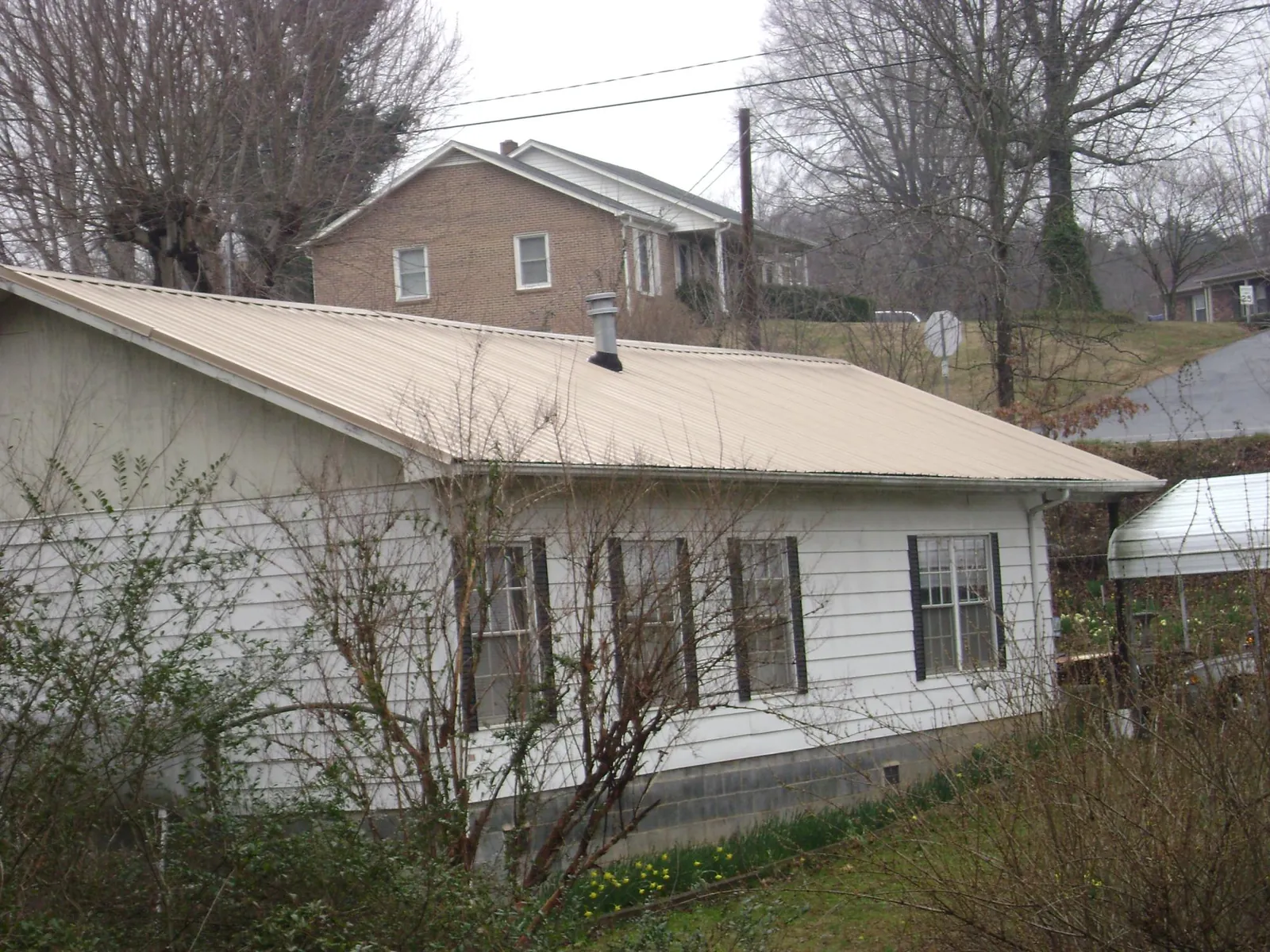 Tan metal roof on a white sided house set into a hillside — Commercial Roofing by Roofing Brothers in Newry