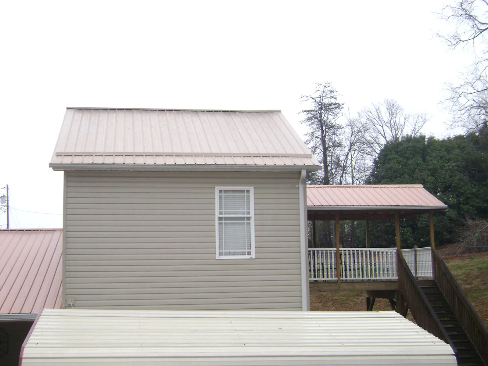 Tan metal roofs on a two story addition and attached porch, from a Roof Replacement job in Newry
